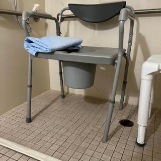 A commode chair designed for accessibility in a bathroom setting.