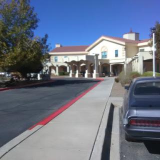 A view of a building with a driveway, flanked by trees under a clear blue sky.