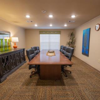 A well-lit conference room with a central wooden table surrounded by chairs, artwork on the walls, and window blinds.
