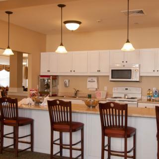 A modern kitchen with a row of barstools at the counter and white cabinets, illuminated by pendant lights.