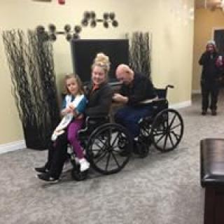 A family sitting together on a wheelchair indoors, sharing a moment of togetherness.
