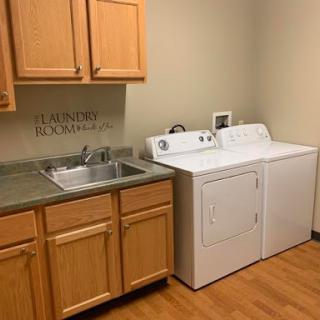 A functional laundry room featuring a washing machine, dryer, and sink with wooden cabinets above.