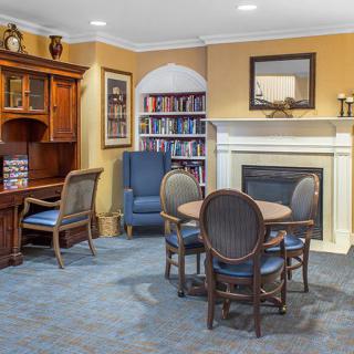 A cozy living room with a library corner, featuring a fireplace, bookshelf, wooden desk, and seating area.