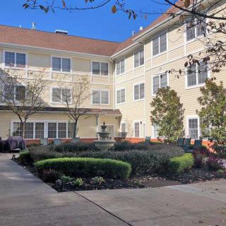 A view of a residential building with a landscaped garden and trees under a clear blue sky.