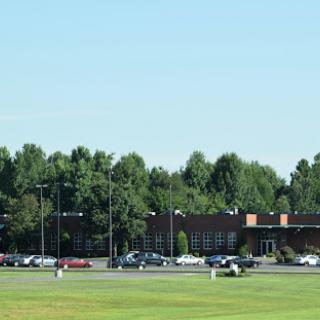 A view of a school building surrounded by trees and a parking lot on a clear day.