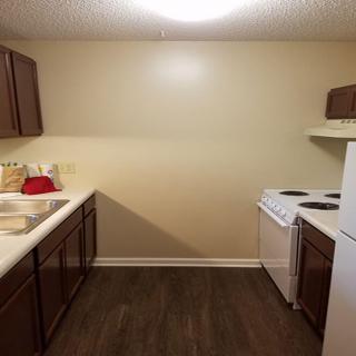 A small kitchen with a stove, refrigerator, and wooden cabinets.