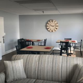 A cozy living room with a dining area featuring a sofa, tables set for dining, and a decorative wall clock.