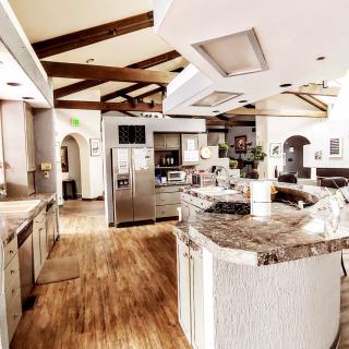 A spacious modern kitchen with an open layout, featuring wooden flooring, marble countertops, and stainless steel appliances.