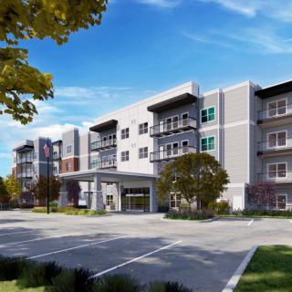 A modern residential apartment building with a parking lot and landscaped surroundings under a partly cloudy sky.
