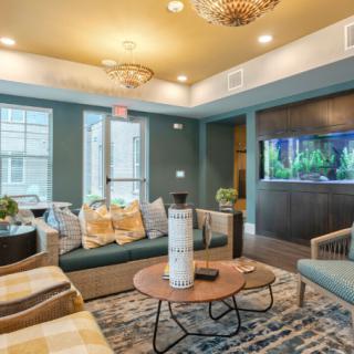 A modern living room with stylish seating, a central coffee table, elegant chandeliers, and an illuminated aquarium.