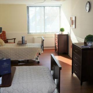 A well-lit hospital room with two beds and furniture.