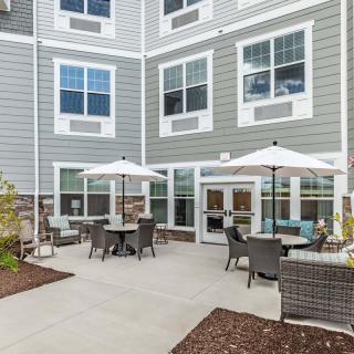A cozy outdoor patio area with tables, chairs, and umbrellas adjacent to a residential building.