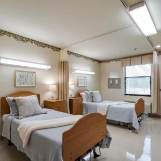 A hospital room with two neatly made beds and bright overhead lighting.