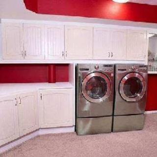 A modern laundry room featuring a washer and dryer set, surrounded by white cabinets and a red accent wall.