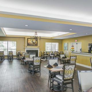 A well-lit dining room with elegant decor, featuring multiple tables and chairs, a fireplace, and large windows.