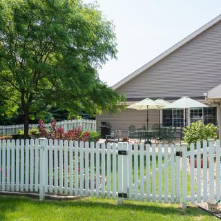 A cozy backyard with a white picket fence, patio furniture, and umbrellas.