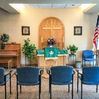 A small chapel with an altar, seating, and a piano, featuring a large cross and an American flag.