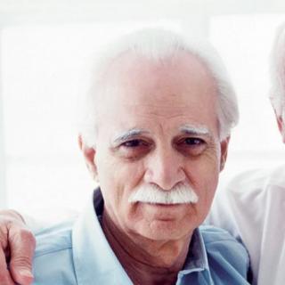 An elderly man with white hair and a mustache, wearing casual clothing indoors.
