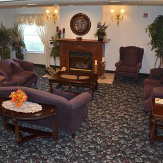 A cozy living room with a fireplace, couches, and armchairs arranged on a patterned carpet.
