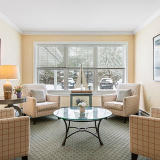 A cozy living room with comfortable armchairs and a coffee table, illuminated by natural light from a large window.