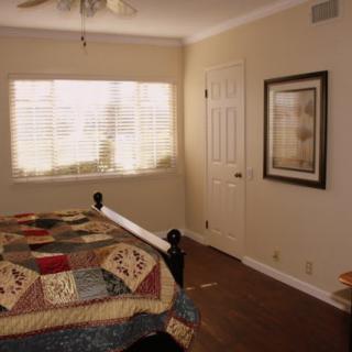 A cozy bedroom with a colorful quilt, large window with blinds, and wall art.
