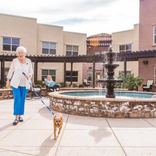 A senior woman walks her dog in a courtyard with a fountain at a retirement home.