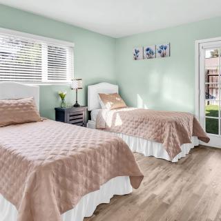 A bright and modern bedroom featuring two twin beds with beige covers and light wood flooring.
