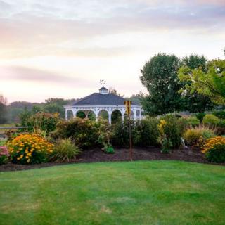 A beautiful garden with a gazebo surrounded by vibrant flowers and lush greenery at sunset.