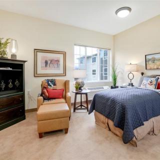 A cozy bedroom with a comfortable armchair, neatly made bed, and decorative artwork on the walls.