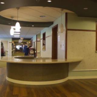 A hospital corridor with a central reception desk and overhead lighting.