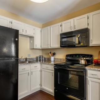 A modern kitchen with white cabinets and black appliances, featuring a stove, refrigerator, and microwave.