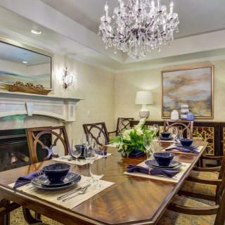 An elegant dining room with a large wooden table set for dinner, a chandelier overhead, and tasteful decor including a fireplace and artwork.