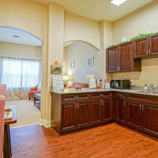 A cozy kitchen with wooden cabinets and modern appliances, featuring an open layout leading to a well-lit living area.