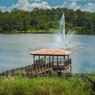 A serene lake view with a gazebo and fountain surrounded by lush greenery.