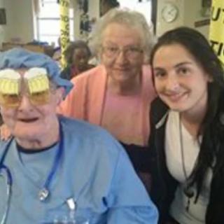 A cheerful group photo with an elderly man wearing humorous glasses and two women in a hospital setting.
