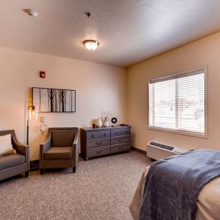 A cozy hotel room with an armchair near a window, a bed, and a dresser.