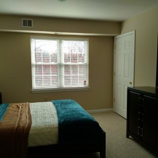A cozy bedroom with a neatly made bed, dresser, and large window.
