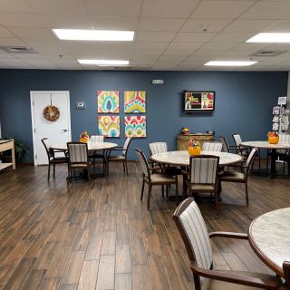 A cozy dining area with round tables and chairs, decorated with colorful artwork on the walls.