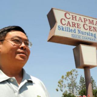 A person stands outside near a sign for Chapman Care Center on a sunny day.