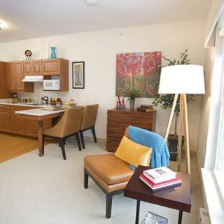 A cozy apartment interior featuring a living room and kitchen with warm-toned furniture and decor.