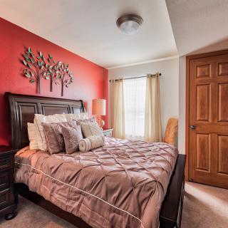 A cozy bedroom with a warm red accent wall, stylish bedding, and natural light streaming through the window.