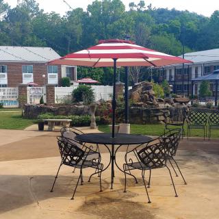 A patio setup with a table, chairs, and a striped umbrella in a garden setting.