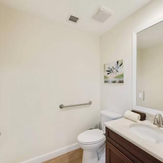 A minimalist bathroom featuring a toilet, sink with a mirror above, and simple wall art.