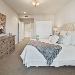 A cozy and elegantly decorated bedroom featuring a large bed with pillows and a throw blanket, complemented by a wooden dresser.