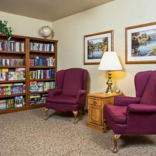 A cozy reading area with purple armchairs, bookshelves, and decorative paintings.