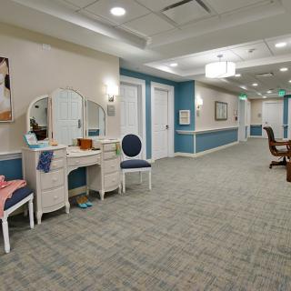 A well-lit hallway featuring a dressing table and chairs with carpeted flooring.
