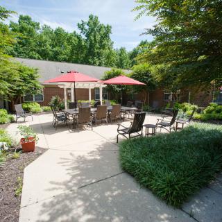 A tranquil patio area with outdoor seating and red umbrellas, surrounded by lush greenery.