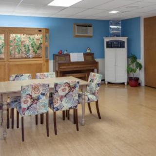 A brightly decorated room with a table, floral chairs, and a piano.