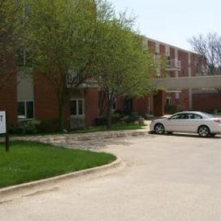 A brick building with a car parked in the driveway surrounded by trees.