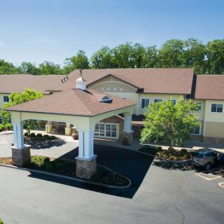 A sunny view of a building entrance surrounded by trees and a parking lot.